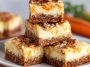Cream cheese bars with carrot cake flavor, topped with creamy frosting and sprinkled with cinnamon, served on a tray with fresh carrot shavings.