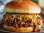 French onion beef sloppy joes topped with melted cheese, served on toasted buns with caramelized onions and savory beef filling, garnished with parsley.