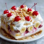 Slice of no bake banana split cake topped with whipped cream, nuts, and a cherry.