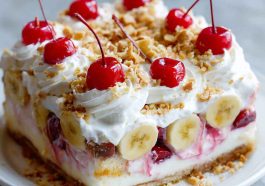 Slice of no bake banana split cake topped with whipped cream, nuts, and a cherry.