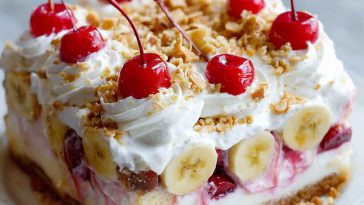 Slice of no bake banana split cake topped with whipped cream, nuts, and a cherry.