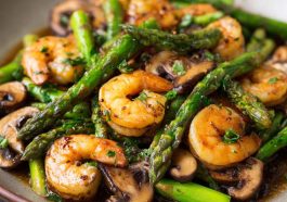 Shrimp and Asparagus Stir-Fry with Mushrooms cooked in a savory sauce, served in a skillet with vibrant green asparagus and tender shrimp.