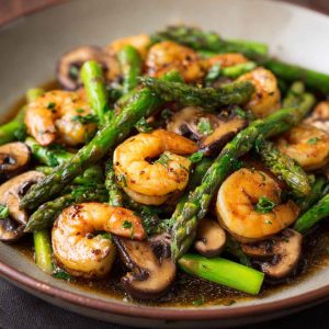 Shrimp and Asparagus Stir-Fry with Mushrooms cooked in a savory sauce, served in a skillet with vibrant green asparagus and tender shrimp.