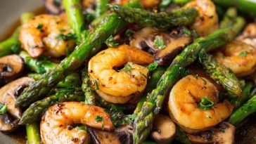 Shrimp and Asparagus Stir-Fry with Mushrooms cooked in a savory sauce, served in a skillet with vibrant green asparagus and tender shrimp.