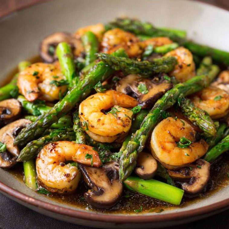 Shrimp and Asparagus Stir-Fry with Mushrooms cooked in a savory sauce, served in a skillet with vibrant green asparagus and tender shrimp.