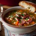 Hearty ham and bean soup with tender beans, smoky ham chunks, carrots, celery, and herbs simmered in a savory broth, served in a rustic bowl.