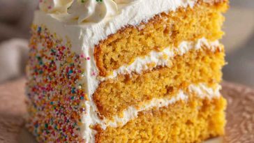 Cornbread cake topped with fluffy whipped honey buttercream frosting, baked golden brown and garnished with a drizzle of honey and fresh herbs for a rustic presentation.