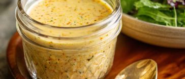 Parmesan vinaigrette salad dressing in a glass jar, creamy and bold with grated parmesan, olive oil, garlic, and herbs, served alongside a fresh green salad.