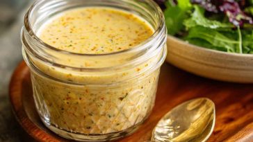 Parmesan vinaigrette salad dressing in a glass jar, creamy and bold with grated parmesan, olive oil, garlic, and herbs, served alongside a fresh green salad.
