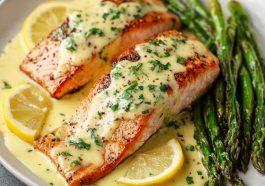 Baked salmon fillet topped with creamy lemon butter sauce, garnished with fresh parsley and lemon slices, served with roasted vegetables.