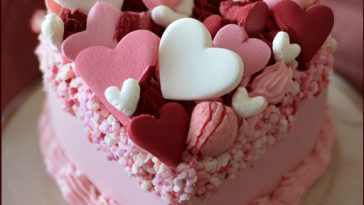 Homemade Valentines Day cakes decorated with pink and red frosting, heart-shaped designs, and festive sprinkles arranged beautifully on a dessert table.