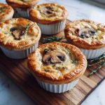 Mini mushroom and Gruyère pot pies baked golden brown with flaky pastry crust, creamy mushroom filling, and melted Gruyère cheese served in ramekins.