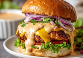 Ultimate smash burger sauce served in a small bowl, creamy and tangy, with a spoon beside juicy smash burgers topped with lettuce, tomato, and cheese.