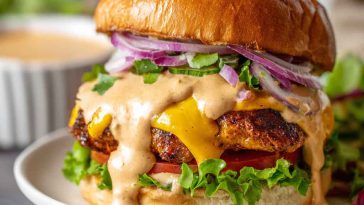 Ultimate smash burger sauce served in a small bowl, creamy and tangy, with a spoon beside juicy smash burgers topped with lettuce, tomato, and cheese.