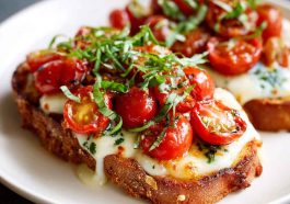 Tomato basil mozzarella toast made with crusty bread topped with fresh mozzarella, ripe tomato slices, basil leaves, and a drizzle of olive oil, served golden and crisp.