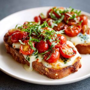 Tomato basil mozzarella toast made with crusty bread topped with fresh mozzarella, ripe tomato slices, basil leaves, and a drizzle of olive oil, served golden and crisp.