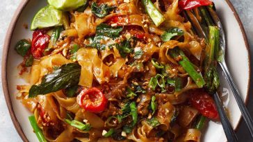 Street style Thai drunken noodles stir-fried in a wok, with wide rice noodles, colorful bell peppers, Thai basil, and chili sauce, served hot and spicy.
