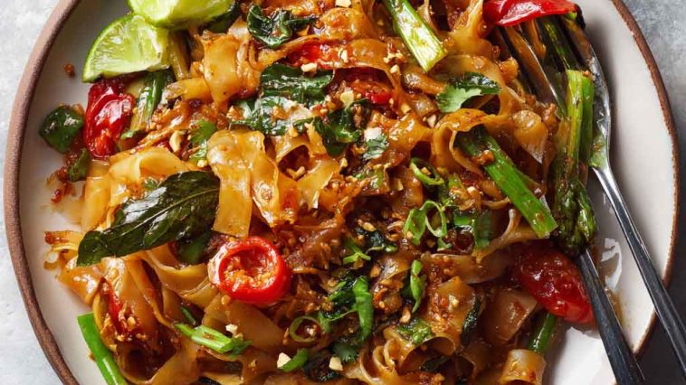 Street style Thai drunken noodles stir-fried in a wok, with wide rice noodles, colorful bell peppers, Thai basil, and chili sauce, served hot and spicy.