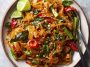 Street style Thai drunken noodles stir-fried in a wok, with wide rice noodles, colorful bell peppers, Thai basil, and chili sauce, served hot and spicy.