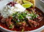 Beef chile colorado served in a rustic bowl with tender beef chunks simmered in a rich red chile sauce, garnished with cilantro and served alongside warm tortillas.
