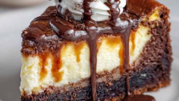 The best brownie cheesecake sliced on a plate, with fudgy brownie layers, creamy cheesecake filling, and a drizzle of chocolate ganache topped with whipped cream.
