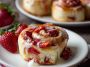 Strawberry Cheesecake Cinnabon Rolls topped with cream cheese frosting and fresh strawberry glaze, served on a dessert plate.