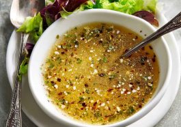 Homemade parmesan vinaigrette in a glass jar with fresh parmesan cheese, olive oil, and herbs on a wooden table.