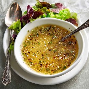 Homemade parmesan vinaigrette in a glass jar with fresh parmesan cheese, olive oil, and herbs on a wooden table.