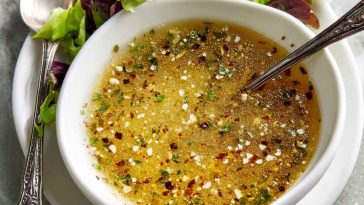 Homemade parmesan vinaigrette in a glass jar with fresh parmesan cheese, olive oil, and herbs on a wooden table.