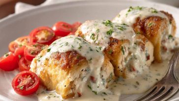 Golden chicken pillows filled with creamy cheese, topped with rich Parmesan sauce, served on a rustic plate with fresh herbs.