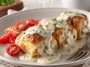 Golden chicken pillows filled with creamy cheese, topped with rich Parmesan sauce, served on a rustic plate with fresh herbs.