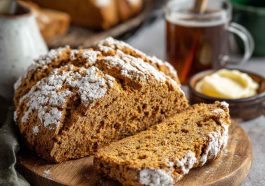 A rustic loaf of brown soda bread sliced on a wooden board, showing its hearty texture and golden crust.