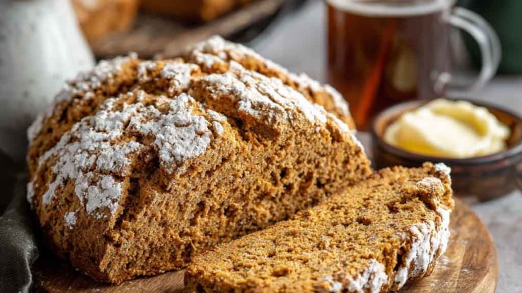 A rustic loaf of brown soda bread sliced on a wooden board, showing its hearty texture and golden crust.