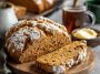 A rustic loaf of brown soda bread sliced on a wooden board, showing its hearty texture and golden crust.