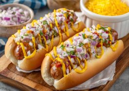 Juicy grilled hot dogs topped with spicy firecracker sauce, garnished with fresh herbs, served on a toasted bun.