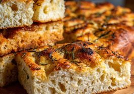 Golden sourdough focaccia bread topped with rosemary, olive oil, and sea salt on a wooden board