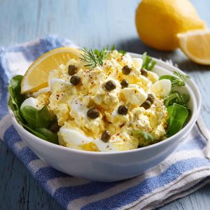 Creamy lemon caper egg salad served in a bowl with fresh herbs and crusty bread slices on the side