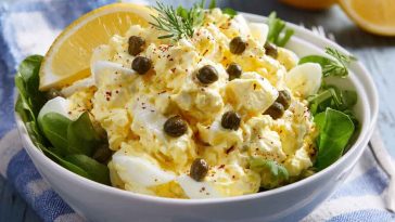 Creamy lemon caper egg salad served in a bowl with fresh herbs and crusty bread slices on the side
