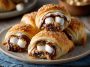 Golden crescent rolls filled with melted chocolate, gooey marshmallows, and graham cracker crumbs, served warm on a plate.