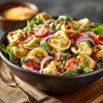 Colorful tortellini salad with cherry tomatoes, olives, fresh herbs, and shredded cheese, served in a large salad bowl.