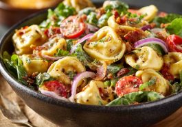 Colorful tortellini salad with cherry tomatoes, olives, fresh herbs, and shredded cheese, served in a large salad bowl.