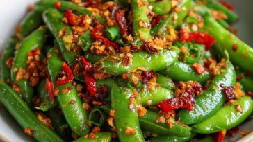 Crisp snap peas tossed in spicy chili crisp sauce with sesame seeds and fresh herbs, served in a white salad bowl.