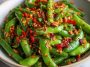 Crisp snap peas tossed in spicy chili crisp sauce with sesame seeds and fresh herbs, served in a white salad bowl.