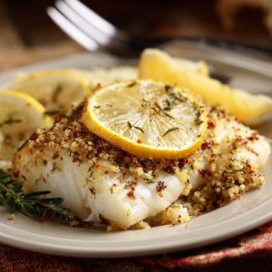 Gluten‑free Mediterranean baked cod fillets topped with lemon slices, garlic, and fresh herbs served in a baking dish.