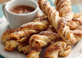 Golden melt‑in‑your‑mouth cinnamon twists with flaky layers, dusted with cinnamon sugar and drizzled with icing on a rustic tray.