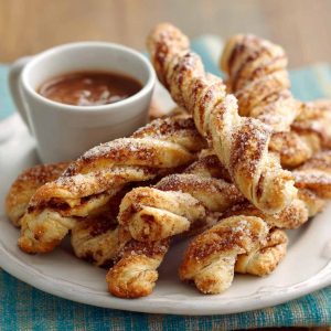 Golden melt‑in‑your‑mouth cinnamon twists with flaky layers, dusted with cinnamon sugar and drizzled with icing on a rustic tray.