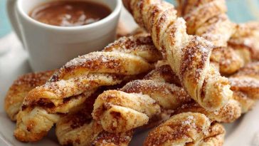 Golden melt‑in‑your‑mouth cinnamon twists with flaky layers, dusted with cinnamon sugar and drizzled with icing on a rustic tray.