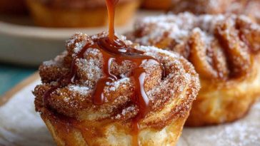 Churro Cruffins with golden, flaky layers coated in cinnamon sugar and drizzled with caramel sauce, served on a plate.