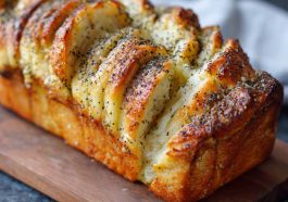 Golden pull-apart bread layered with lemon glaze and sprinkled with poppy seeds, served on a rustic plate.