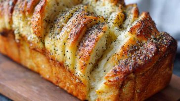 Golden pull-apart bread layered with lemon glaze and sprinkled with poppy seeds, served on a rustic plate.